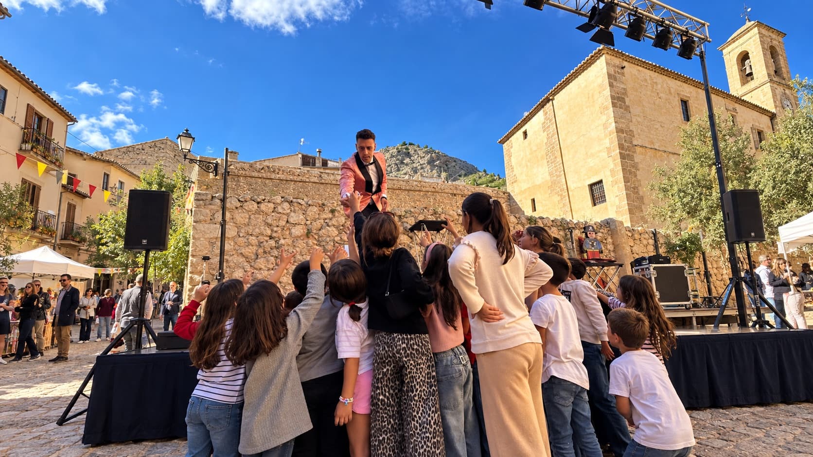 Alexander Main a l'escenari d'una plaça envoltat de nens durant unes festes